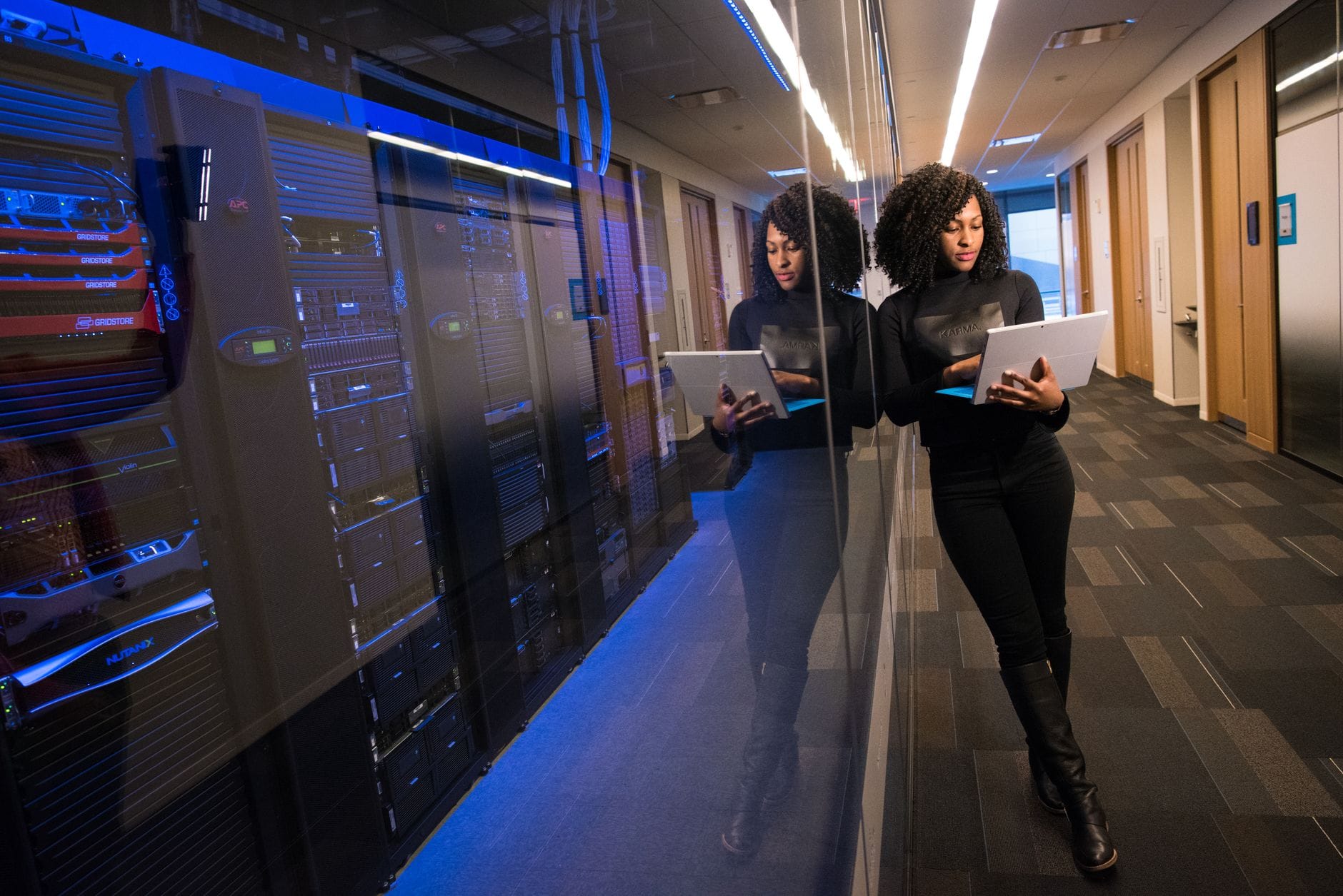 Kobieta z laptopem idzie między lustrzanymi serwerami w data center